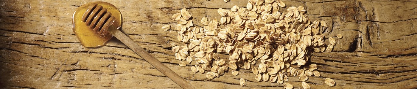 Avena sparsa su una superficie di legno, accanto a un salsiera con miele.