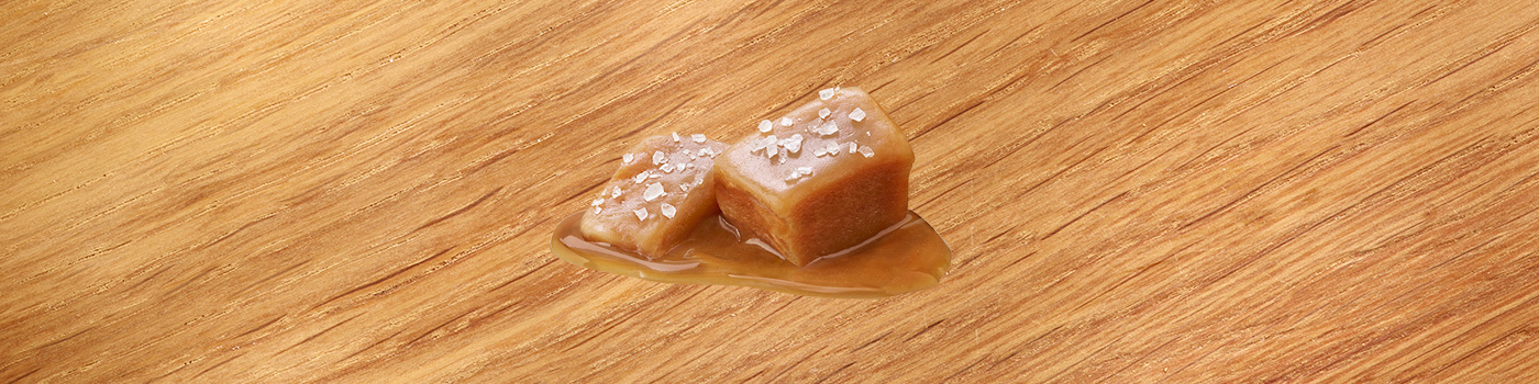 Due caramelle al caramello ricoperte di sale marino si trovano su una superficie di legno, parzialmente sciolte.