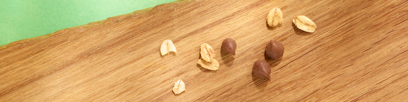Tre nocciole intere e diversi pezzi di avena sono sparsi su una superficie di legno con sfondo verde.